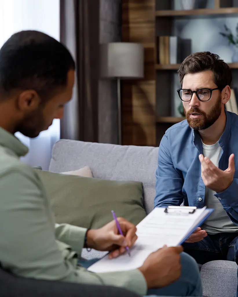 Therapist attentively taking notes while the patient speaks, ensuring optimal care through Health Net psychological services coverage during individual therapy.